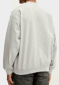 Sudadera gris claro con cuello redondo, puños y dobladillo acanalados, y textura suave. Presenta un ajuste relajado y un diseño casual.