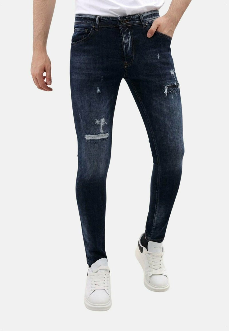 Slank gesneden donkerblauwe jeans met versleten details en lichte vervaging. Gemaakt van denim, met meerdere scheuren en een klassieke vijf-pocketstijl.