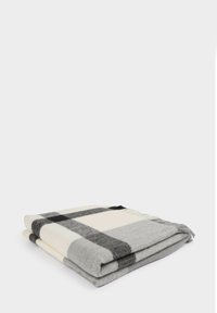 Coperta in lana piegata con motivo a quadri grigio, nero e crema, e frange corte su un lato, posizionata su una superficie bianca.