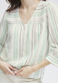 Blusa leggera a righe con scollo a V, caratterizzata da linee verdi, viola e bianche. Chiusura con bottoni e maniche a tre quarti. Texture morbida.