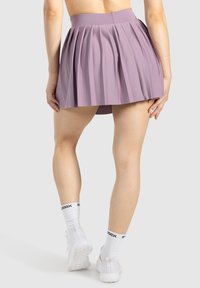 Gonna plissettata viola realizzata in tessuto leggero, con un alta vita e un design svasato, abbinata a scarpe sportive bianche e calzini.