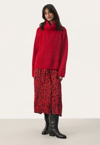 Rode gebreide coltrui gecombineerd met een lange rode rok met een zwart luipaardprint. Zwarte kniehoog laarzen maken de outfit compleet.
