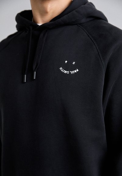Fleece preto feito de algodão, com um bolso frontal, capucho ajustável por cordão e texto bordado em branco com um design de smiley no peito.