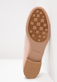 Chaussure Clarks avec un dessus lisse rose clair et une semelle en caoutchouc dotée d'un motif de grip texturé et d'un logo en relief. Forme plate et arrondie.