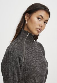 Prilegajoča, temno siva rebrasta jopica z visokim ovratnikom in detajlom srebrnega zadrge. Mehka tekstura, tesno prilegajoča zasnova in pletenina.