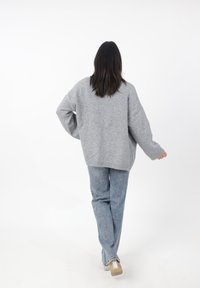 Maglione grigio oversize con una vestibilità rilassata, polsini e orlo a coste, abbinato a jeans blu chiaro a gamba dritta e scarpe con tacco trasparenti.