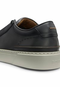 Black leather sneaker with a smooth finish, featuring a low profile, white sole, and minimalistic stitching and accents.