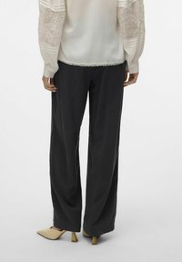 Vloeiende zwarte broek met een ontspannen pasvorm en een gladde textuur, gecombineerd met een lichtbeige blouse met geborduurde mouwen en stroken.