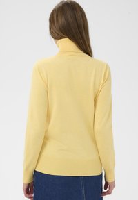 Pull à col roulé jaune avec col et poignets côtelés, en tissu doux, présentant une coupe décontractée et une texture lisse.