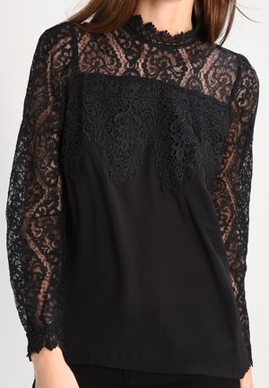 Czarna bluzka z długim rękawem, z przezroczystymi koronkowymi rękawami i górną częścią biustu z misternymi koronkowymi kwiatowymi zdobieniami oraz wysokim koronkowym kołnierzem.