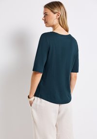 Tmavě modré tričko s krátkým rukávem, zaobleným výstřihem a uvolněným střihem, doplněné světlými volnými kalhotami, které mají jednoduchý design.