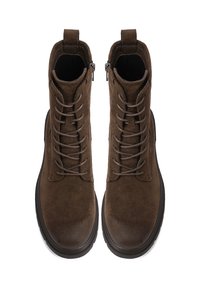 Un paio di stivali alla caviglia in suede marrone, con lacci e cerniere laterali, mostrati dall'alto su uno sfondo bianco.
