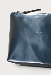 Borsetta impermeabile blu navy con una superficie liscia, dotata di logo "RAINS" in rilievo e una cerniera nera. Forma rettangolare.