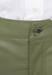 Zielone skórzane spodnie charakteryzują się gładką teksturą, widocznym szwem oraz srebrnym guzikiem z logo "2ND DAY" na pasie.