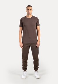 Brązowy t-shirt z krótkim rękawem zestawiony z pasującymi dresami, charakteryzujący się prostym wzorem, gładką teksturą oraz białymi trampkami dla kontrastu.