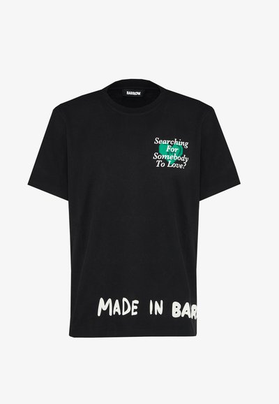 T-shirt in cotone nera con maniche corte. Presenta testo bianco: "FATTO A BARROW" e "Cercando Qualcuno da Amare?" in verde e bianco.