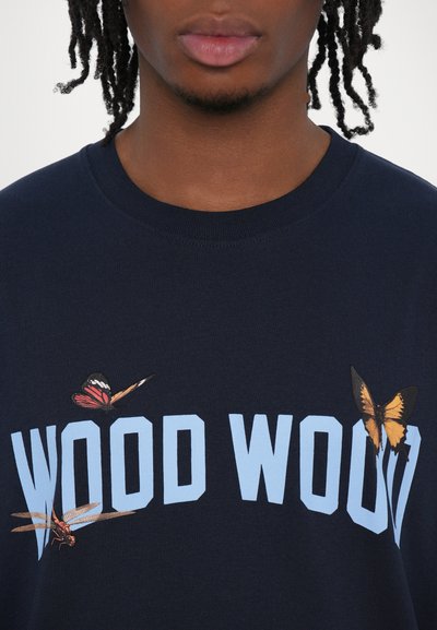 Camiseta de color azul marino con escote de barco que presenta "WOOD WOOD" en azul claro. Mariposas bordadas y una libélula añaden color y detalle.
