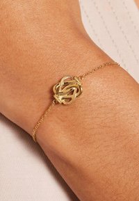 Gold chain bracelet featuring a textured knot design at the center. The chain is fine and delicate, complementing the intricate knotted detail.