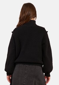 Maglione nero lavorato a maglia con un colletto alto, texture a coste e maniche lunghe e voluminose, caratterizzato da sottili dettagli sulle spalle.