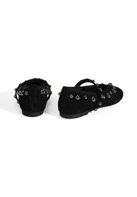 Schwarze Wildlederschuhe mit flachem Design und einem Riemen. Hervorstechend durch metallische, kugelförmige Akzente an der Seite und Rückseite.