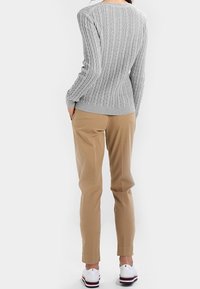 Grijze geribbelde gebreide trui met lange mouwen, gecombineerd met lichtbeige broek en witte schoenen met rode en blauwe accenten.