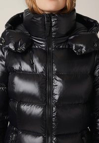 Czarna kurtka puchowa z błyszczącym, pikowanym wykończeniem. Ma wysoki kołnierz, zamek błyskawiczny z przodu oraz napy na ramionach dla dodatkowego akcentu.