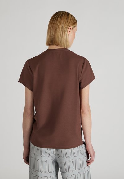 Brązowa bawełniana koszulka z krótkimi rękawami i okrągłym dekoltem, pokazana od tyłu, w zestawie z szarymi spodniami w wzory z prostokątnymi wzorami.