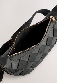Svart läder crossbody-väska med vävt mönster, gulddragkedjestängning och en tygrem. Insidan är fodrad med svart material.