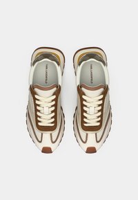 Beige og brune joggesko med en blanding av glatte og strukturerte materialer, med snøring foran og et langstrakt, sporty design.