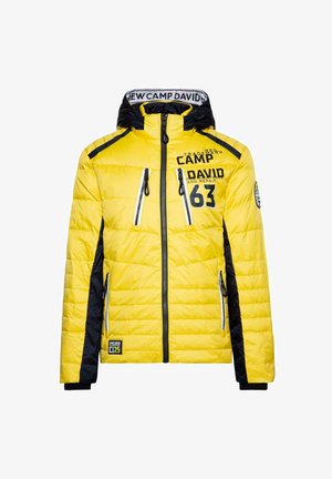 Chaqueta acolchada amarilla con detalles en negro, bolsillos con cremallera, cuello alto y logotipo. Presenta una capucha y puños de canalé.