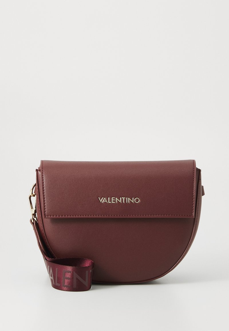 Bolsa transversal de pele bordô com formato arredondado, fecho em aba e logotipo dourado "Valentino". Apresenta uma alça de fita a condizer.