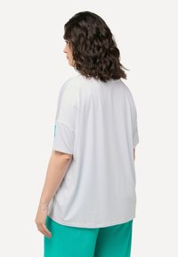 Bílý oversized tričko s krátkými rukávy, s kulatým výstřihem a hladkou, jemnou texturou. Skvěle ladí s tyrkysovými kalhotami.