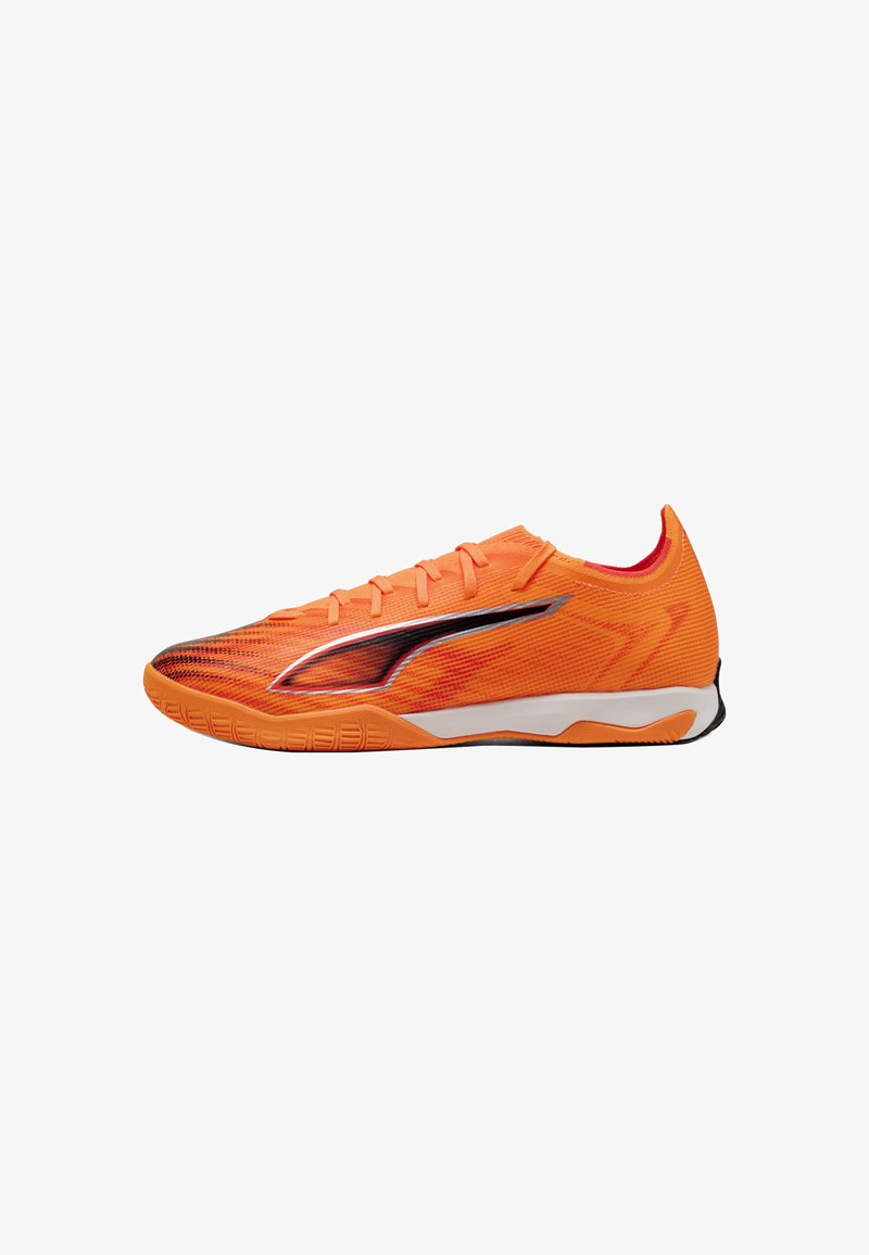 Scarpa sportiva bassa arancione con logo laterale nero e argento, chiusura con lacci e suola bianca e nera, progettata per sport indoor.