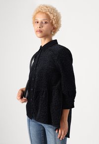 Svart leopardmønstrete skjorte med knappføring foran, krage og puffete ermer; kombinert med lyseblå jeans og en svart veske.