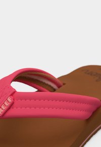 Κλείσιμο λουρίου ροζ σαγιονάρας με ορατή ραφή και καφέ πέλμα, εμφανίζοντας μέρος του ονόματος της μάρκας που είναι ανάγλυφο στο λουρί.