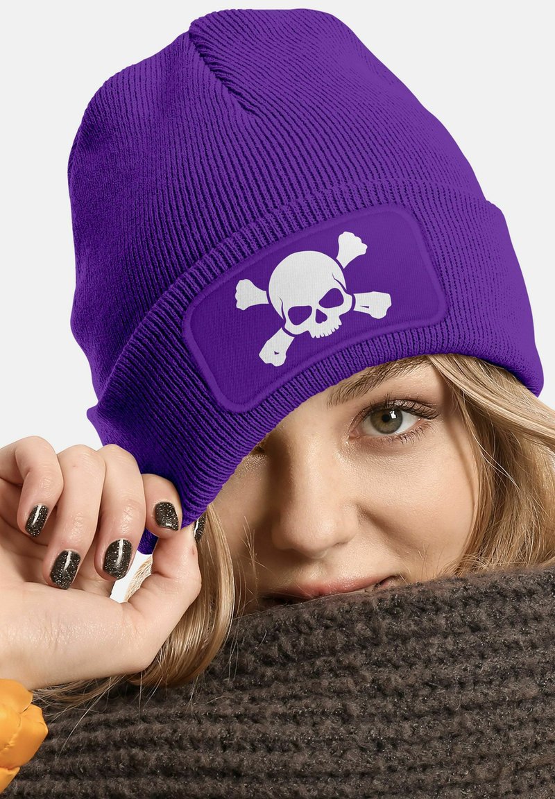 Purple knit beanie featuring a white skull and crossbones graphic on a rectangular patch; ribbed texture with a snug fit.