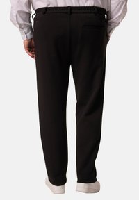 Pantalones negros de corte recto, con cinturilla elástica y bolsillo trasero; textura suave con un diseño minimalista; combinados con zapatillas blancas.