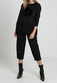 Top nero oversize con design a strati, abbinato a pantaloni neri cropped. Gli accessori includono una piccola borsa nera e stivaletti neri con borchie.