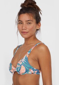 Blommig bikiniöverdel med blå bakgrund, prydd med mönster av rosa och orange blommor. Mjuk tyg, breda axelremmar och triangelformad design.