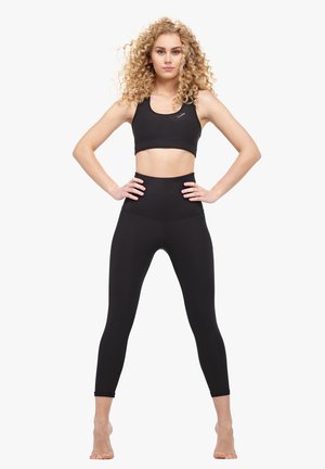 Svart atletisk crop top och högmidjade tights. Tyget är slätt med en elastisk yta. Inga synliga mönster eller hårdvarudetaljer.