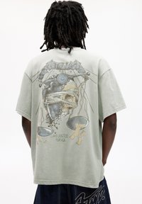 Tricou cu mâneci scurte, de culoare verde deschis, având un design grafic pe spate, care reprezintă un craniu și o balanță, cu textul "...ȘI JUSTIȚIE PENTRU TOȚI."