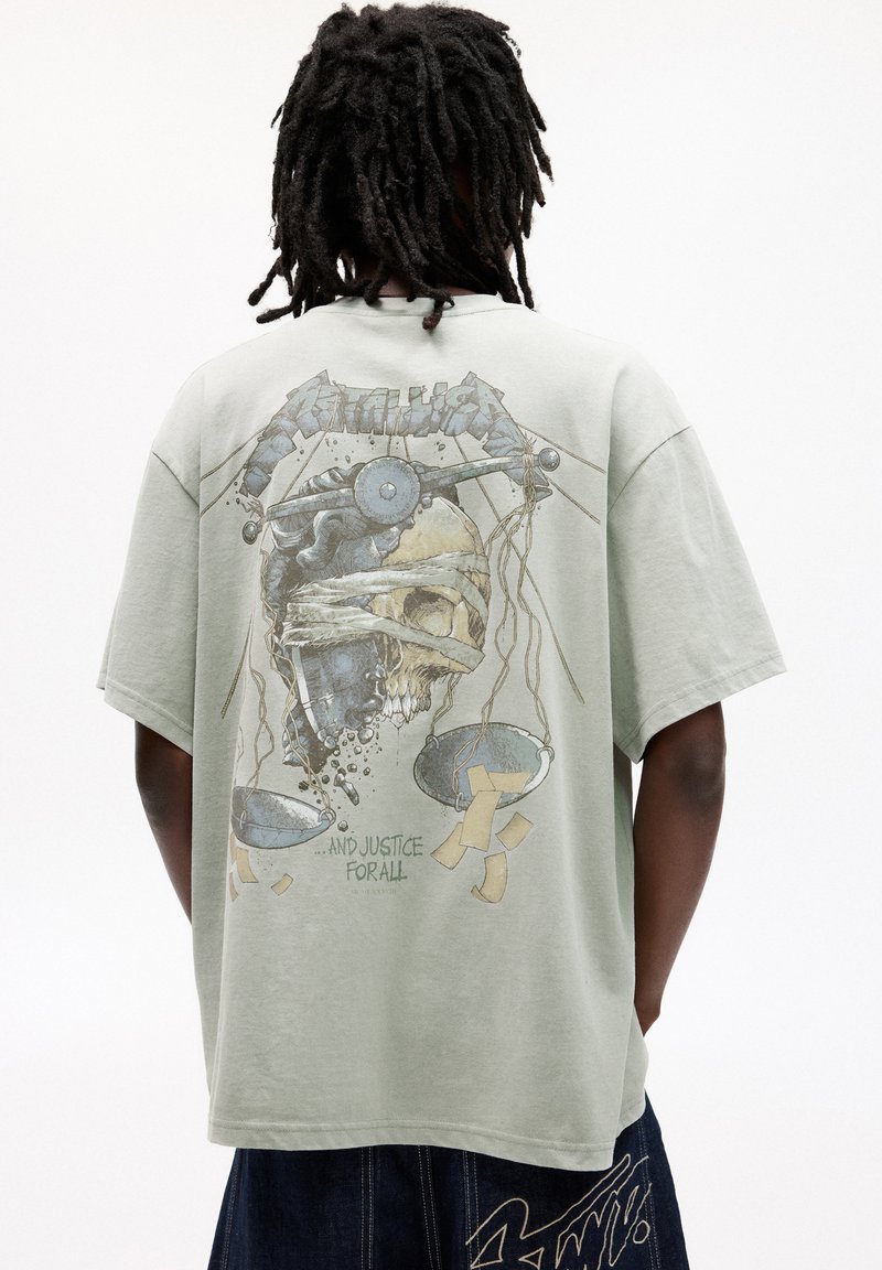Tricou cu mâneci scurte, de culoare verde deschis, având un design grafic pe spate, care reprezintă un craniu și o balanță, cu textul "...ȘI JUSTIȚIE PENTRU TOȚI."