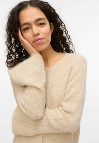 Pull en tricot beige en laine douce et texturée. Doté de manches larges et d'un col rond, avec une coupe ample.