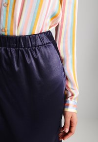 Chemise rayée multicolore avec des boutons, associée à une jupe en satin bleu marine dotée d'une taille élastique, capturant une texture lisse et brillante.