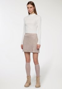 Top bianco a maniche lunghe, gonna A-line in suede beige, calze al ginocchio rosa chiaro e stivali beige con lacci. Texture morbide, design semplice.