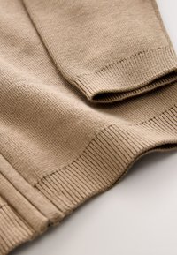 Beige knitted sweater with ribbed cuffs, featuring a textured surface and smooth finish, highlighting a simple, classic design.