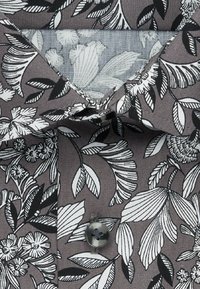 Koszula w kwiatowy wzór na szarym tle, z czarnymi i białymi liśćmi oraz kwiatami. Szczegółowe zapięcie na guziki przy kołnierzu.