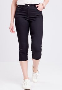 Schwarze Capri-Hosen aus einem dehnbaren Baumwollmischgewebe; mit fünf Taschen und einem vorderen Knopfverschluss. Getragen mit weißen Sneakers.