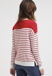 Rood en wit gestreepte trui met lange mouwen, een effen rode bovenkant, ribbelmanchetten en een ronde zoom, gemaakt van zachte gebreide stof.