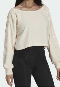 Krämfärgad kort sweatshirt med vid halsringning och långa, texturerade ärmar, kombinerad med svarta leggings. Enkel branding på bröstet.